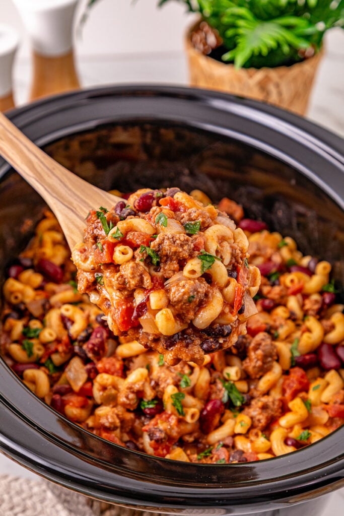 Crockpot chili mac in slow cooker with wooden spoon.