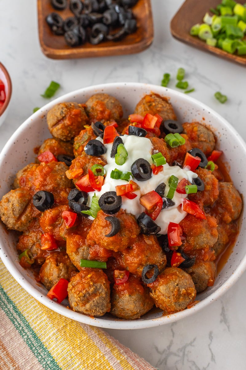 Slow cooker enchilada meatballs in bowl garnished with sour cream, green onions.