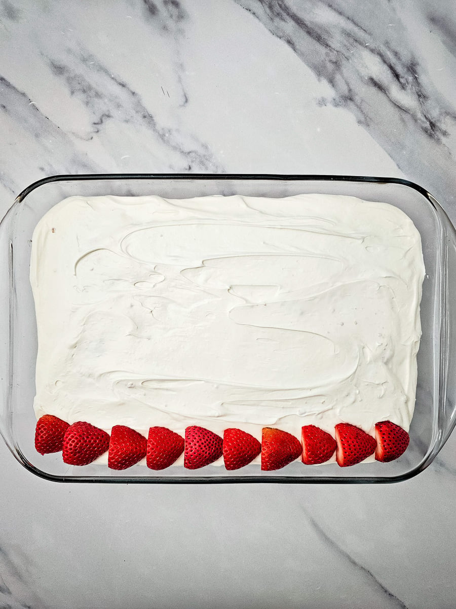 First row of strawberries laid out on top of frosting.