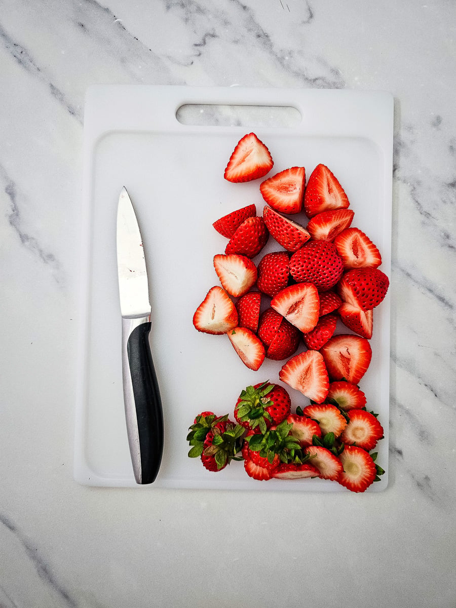 Stems are cut off strwberries and placed on cutting board.