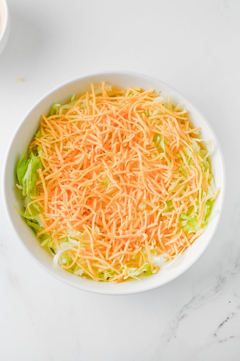 Cheese is sprinkled on top of the lettuce in serving bowl.