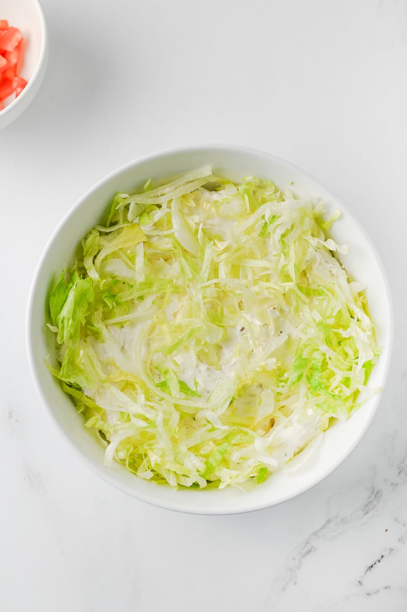 Lettuce is added to the top of the cream cheese mixture in bowl.