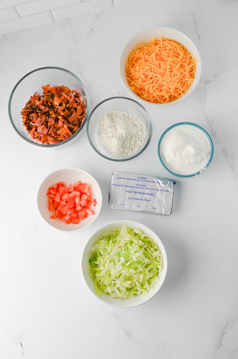 Ingredients for BLT dip in small bowls on counter in preparation for the recipe.