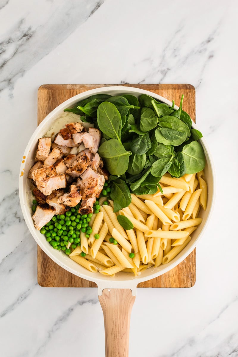 Cooked pasta, spinach, chicken are added to the sauce in the skillet.