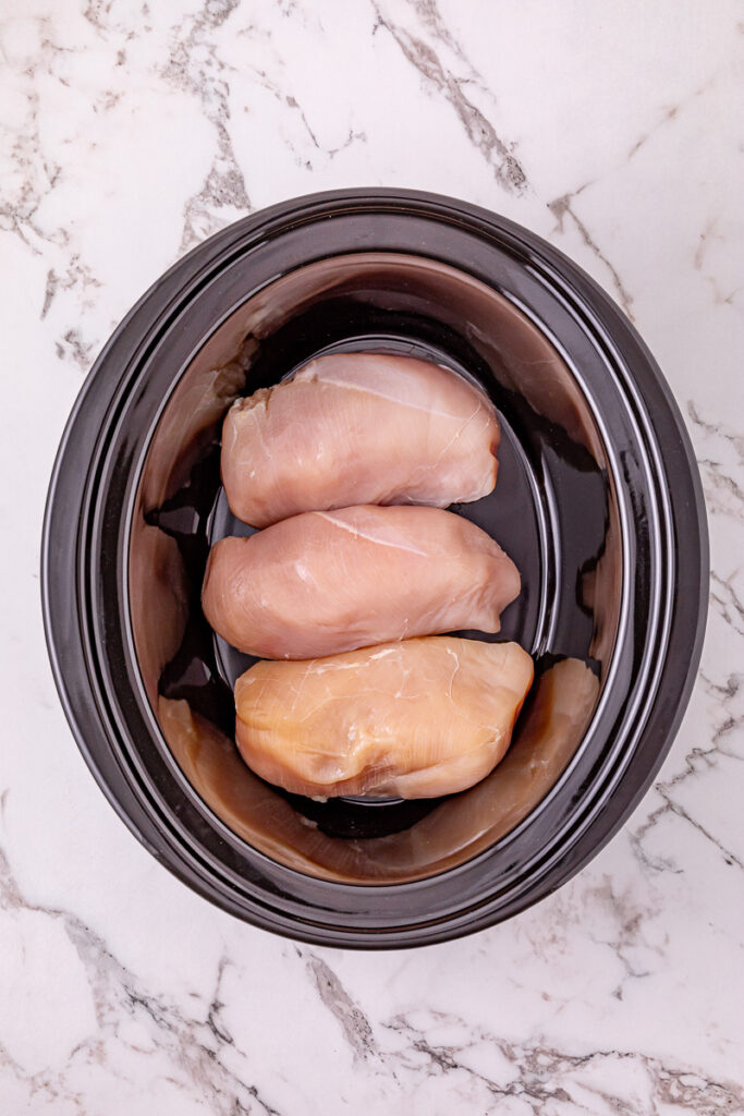 Chicken breasts are placed in bottom of slow cooker.