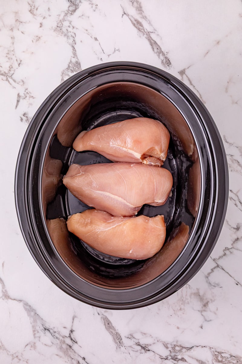 Chicken is placed in the bottom of slow cooker.
