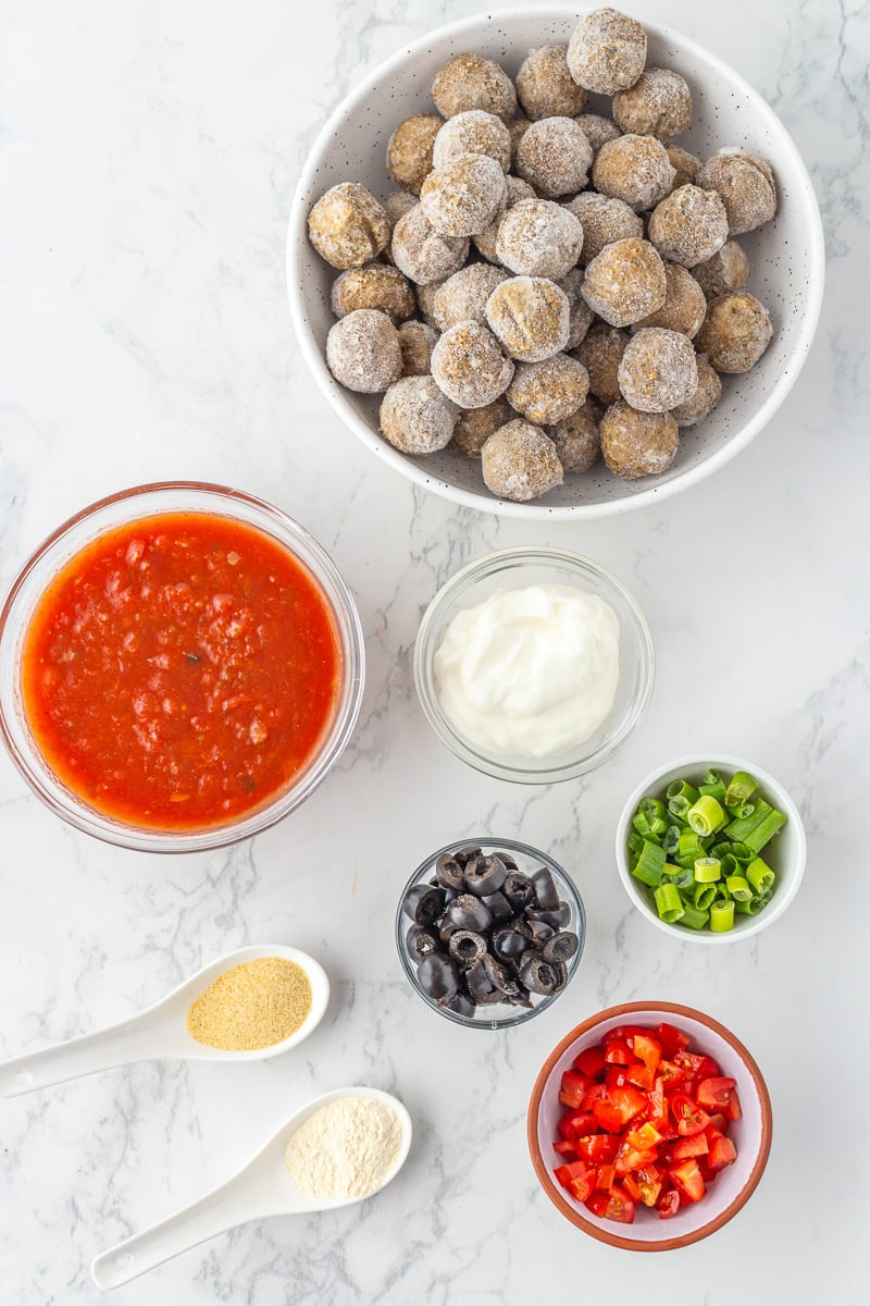 Ingredients for slow cooker enchilada meatballs in small bowls on kitchen counter in prepration for the recipe.