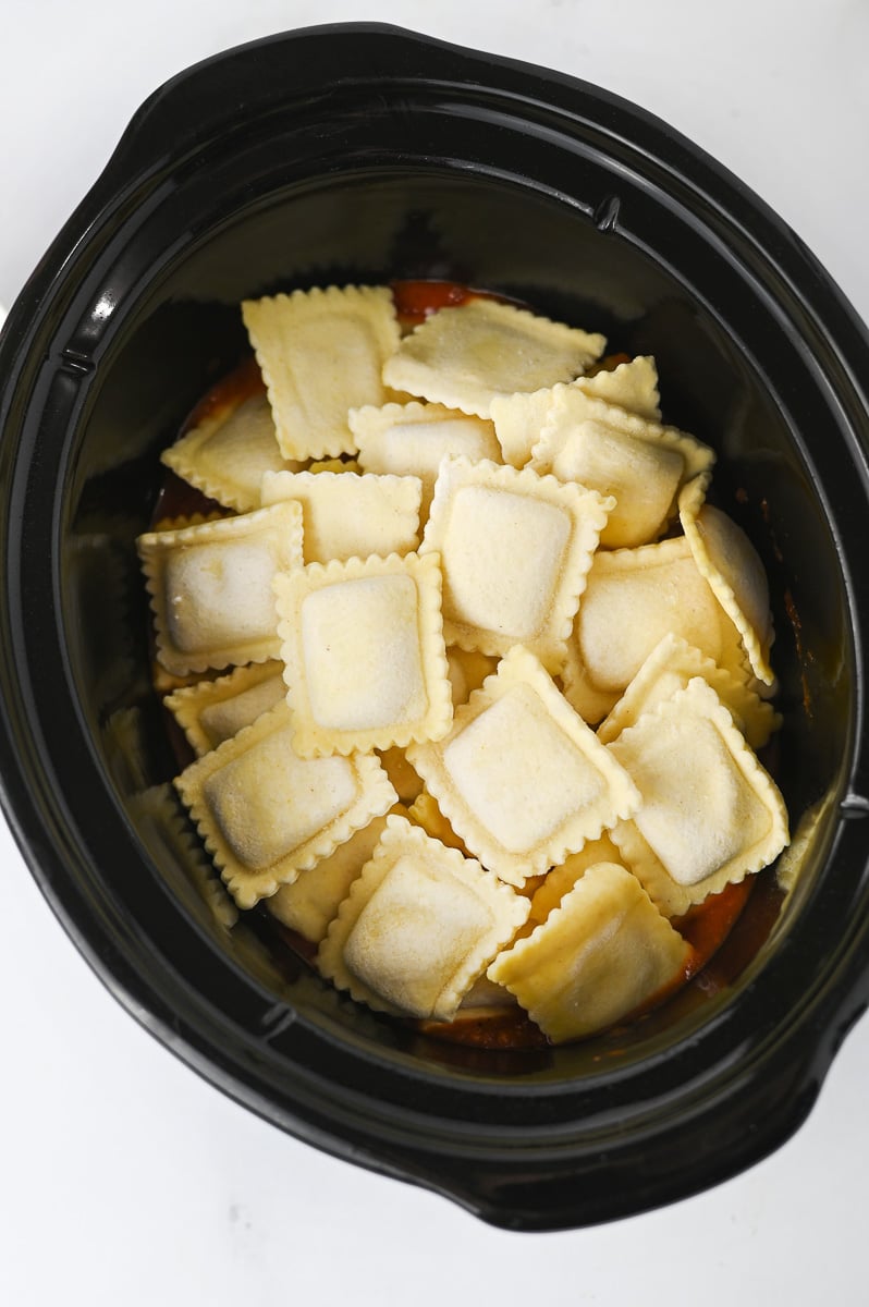 Half of the frozen ravioli is added on top of the sauce in crockpot.