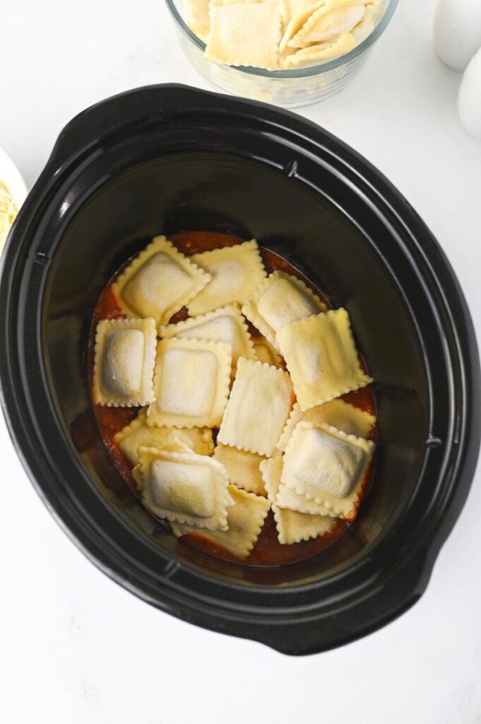Frozen ravioli is placed in bottom of crockpot.