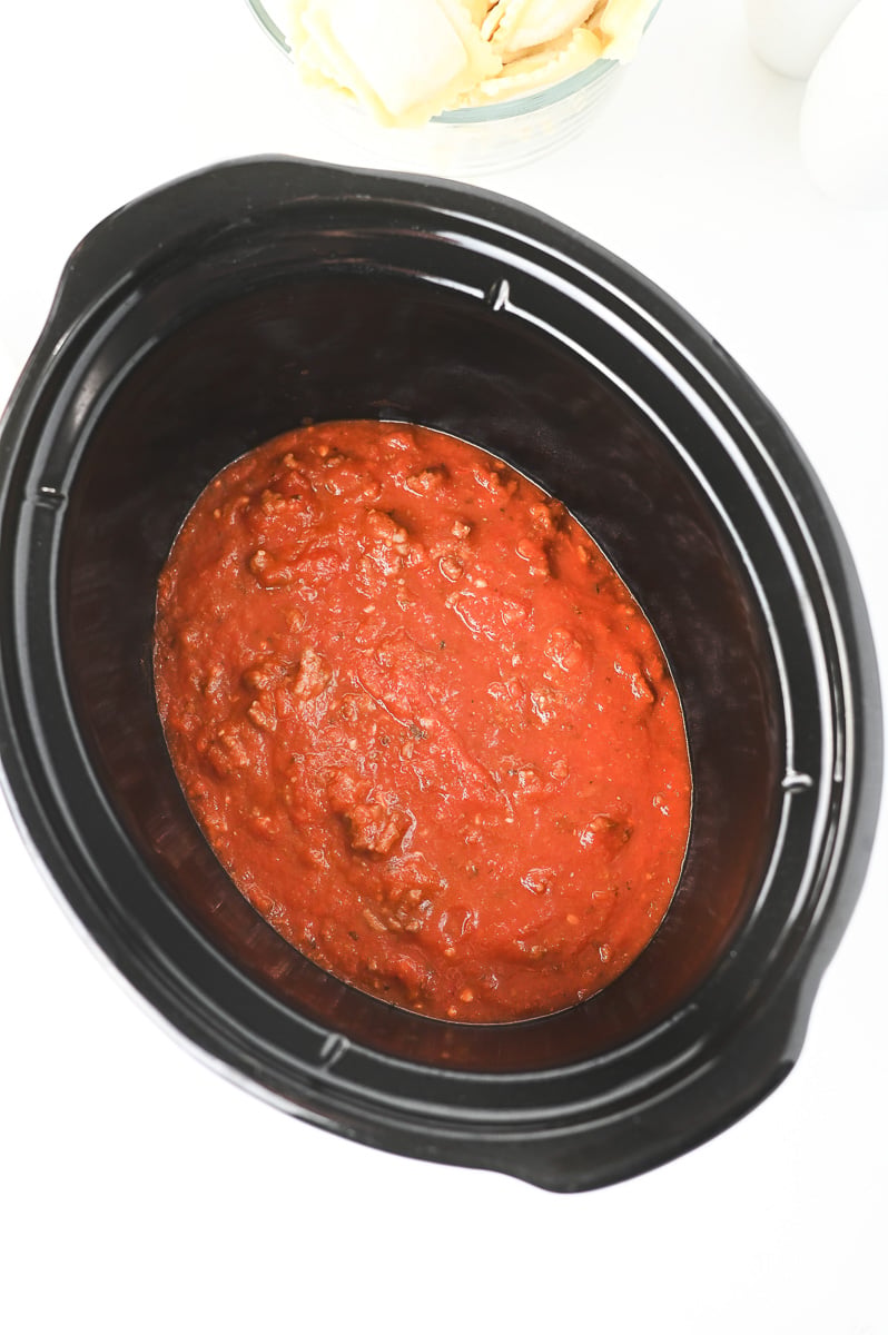 Meat sauce is spread in the bottom of the crockpot.