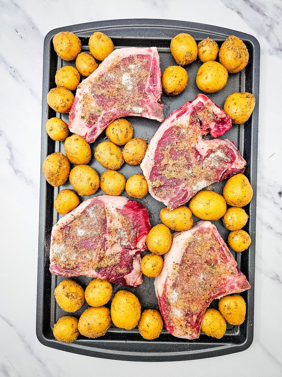 Seasoned potatoes are added to the sheet pan.