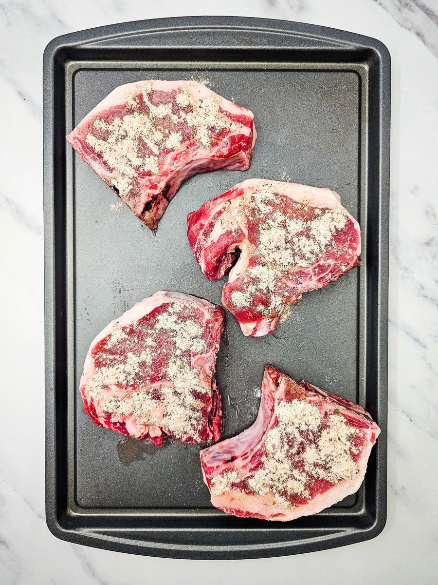 Pork chops on sheet pan with seasoning sprinkled on both sides.