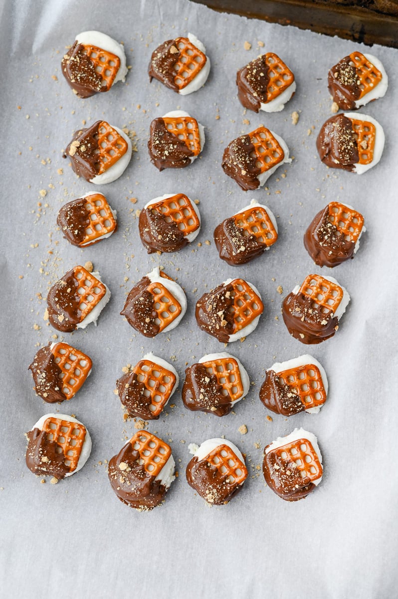Prezels lined on baking shit after having been dipped into chocolate. They are ready to chill.