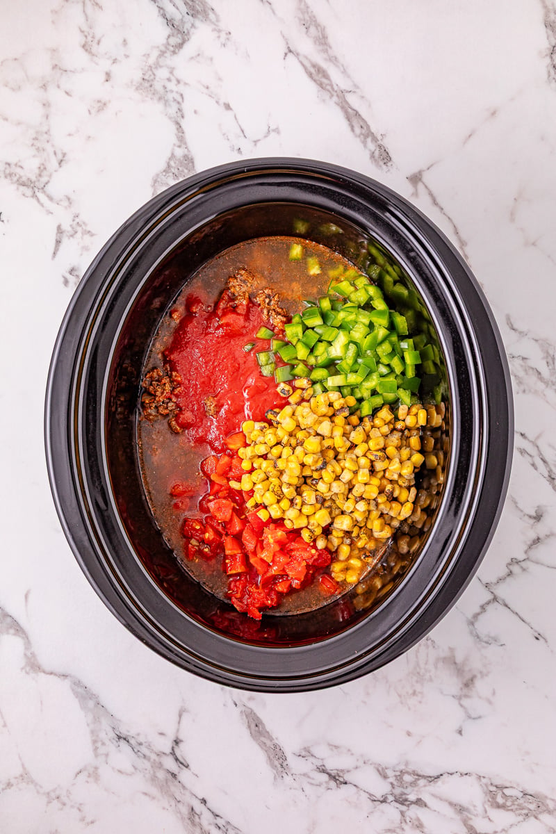 Bell peppers, chicken broth, tomato sauce, diced tomatoes and green chilies, and the frozen corn are added to the ground beef mixture in slow cooker.