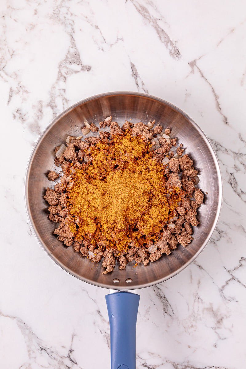 Taco seasoning is added to the skillet with the cooked ground beef.