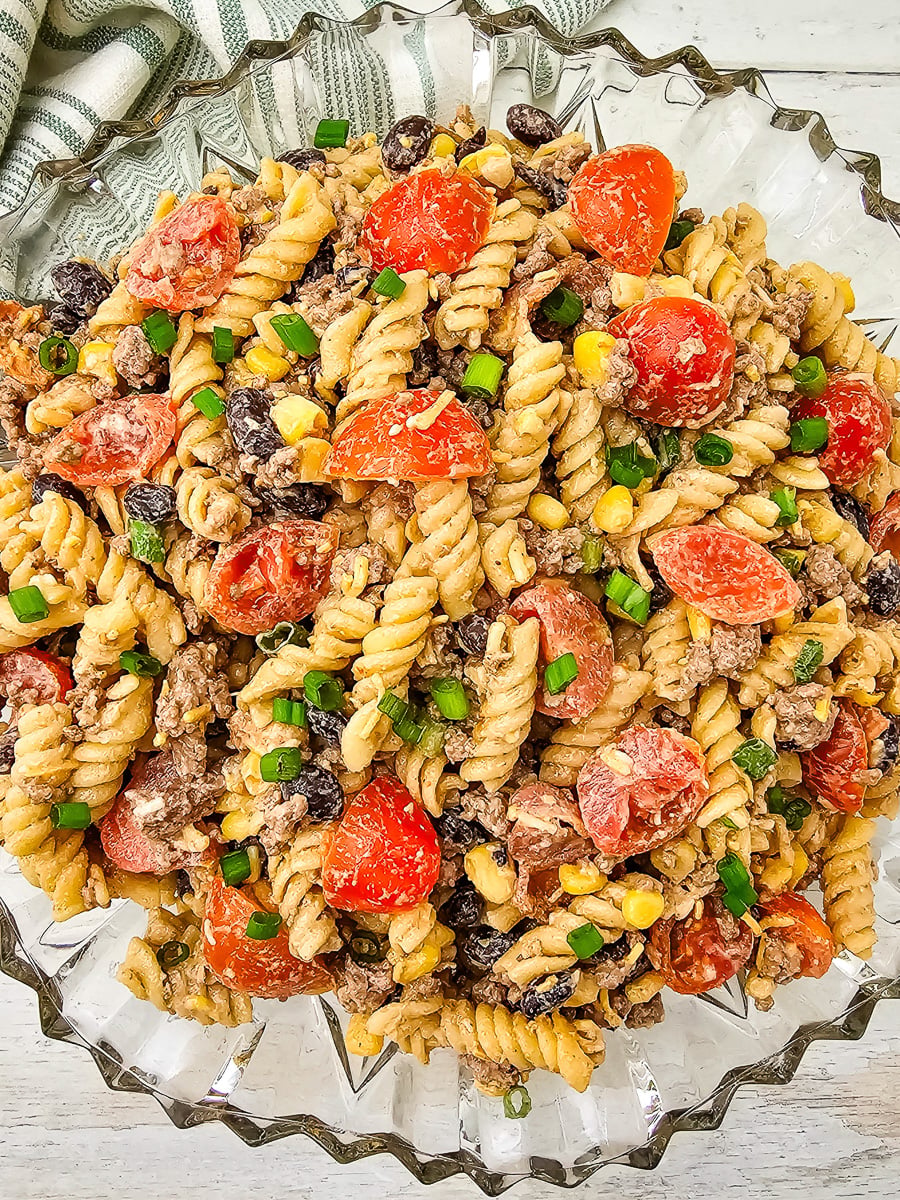 Cowboy pasta salad with ground beef and bacon in a glass bowl for a backyard bbq party.