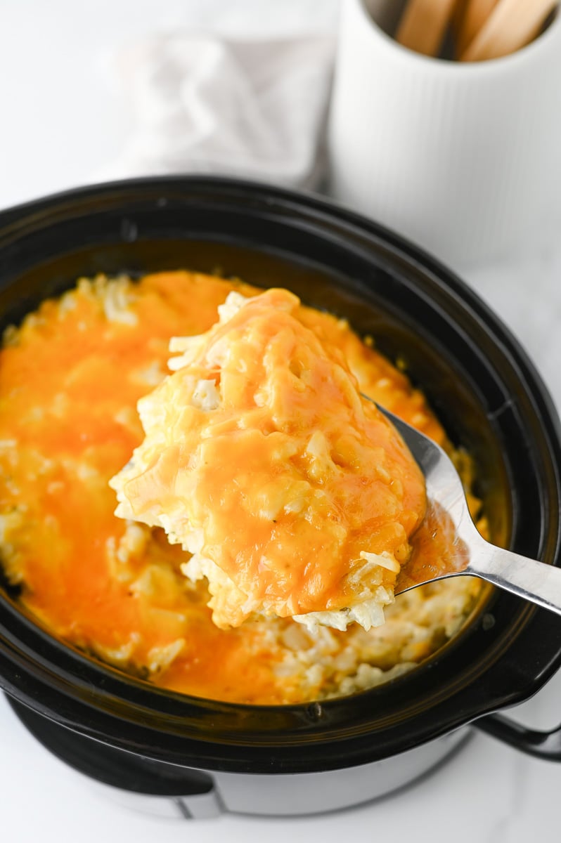 Crockpot hashbrown casserole scooped up on a spoon ready to serve.