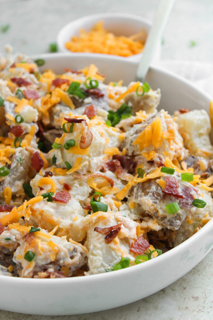 Loaded baked potato salad in a white bowl.