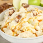 Apple snickers salad, drizzled with caramel sauce in a white bowl.