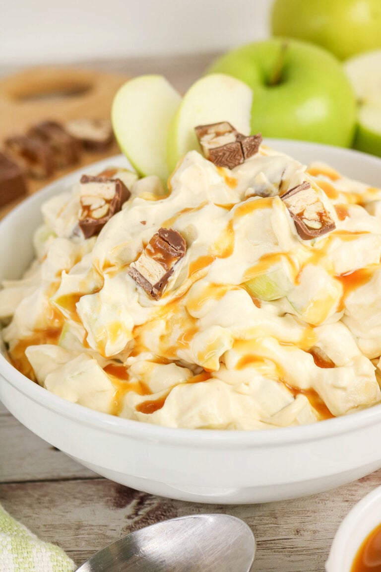Apple snickers salad, drizzled with caramel sauce in a white bowl.