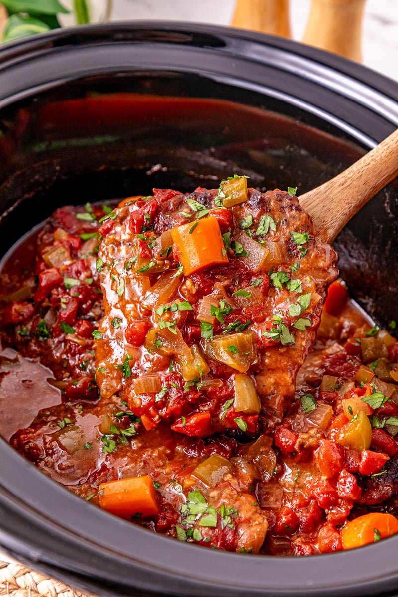 Crockpot Swiss steak held up in serving spoon over the slow cooker.