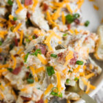 Loaded baked potato salad in a white bowl.