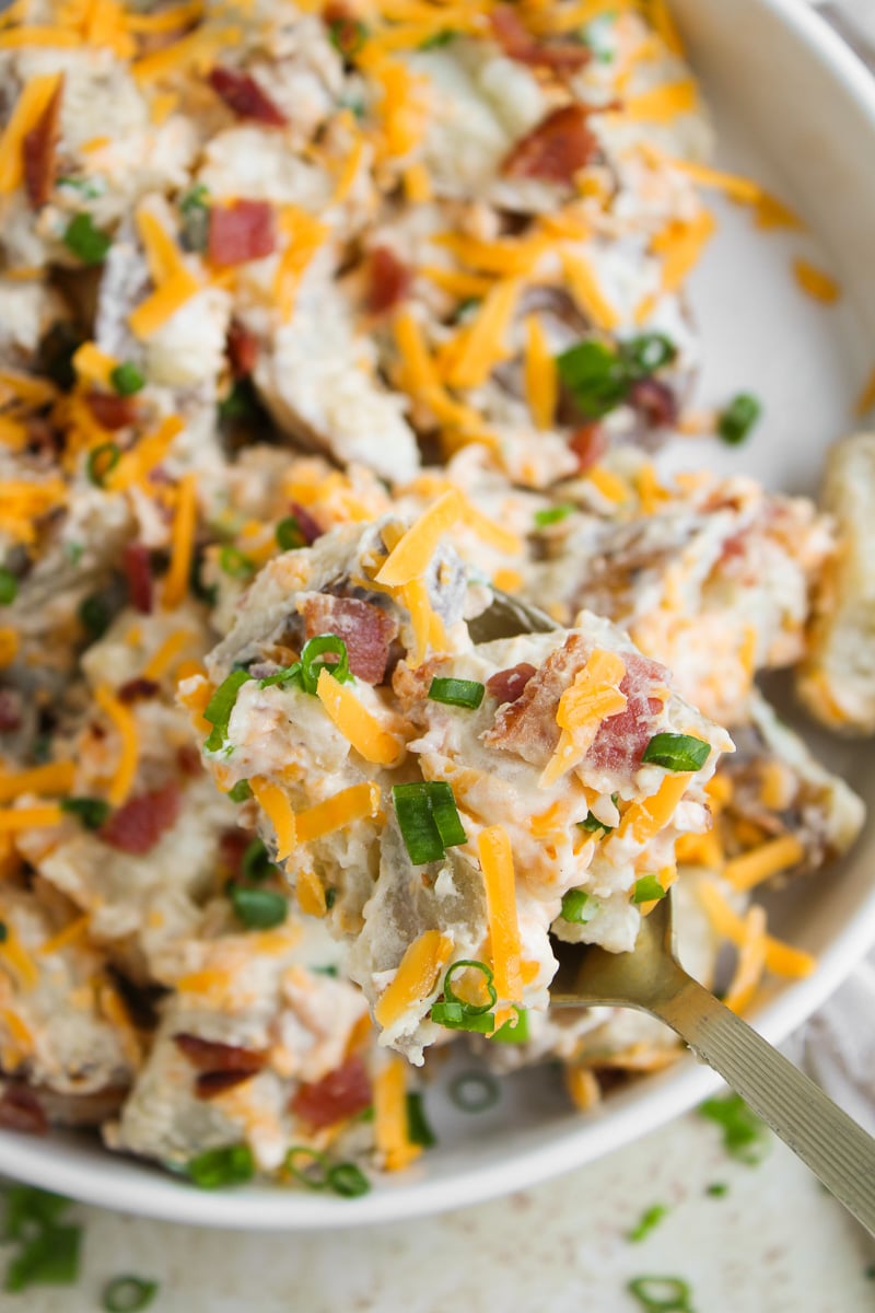 Loaded baked potato salad in a white bowl.