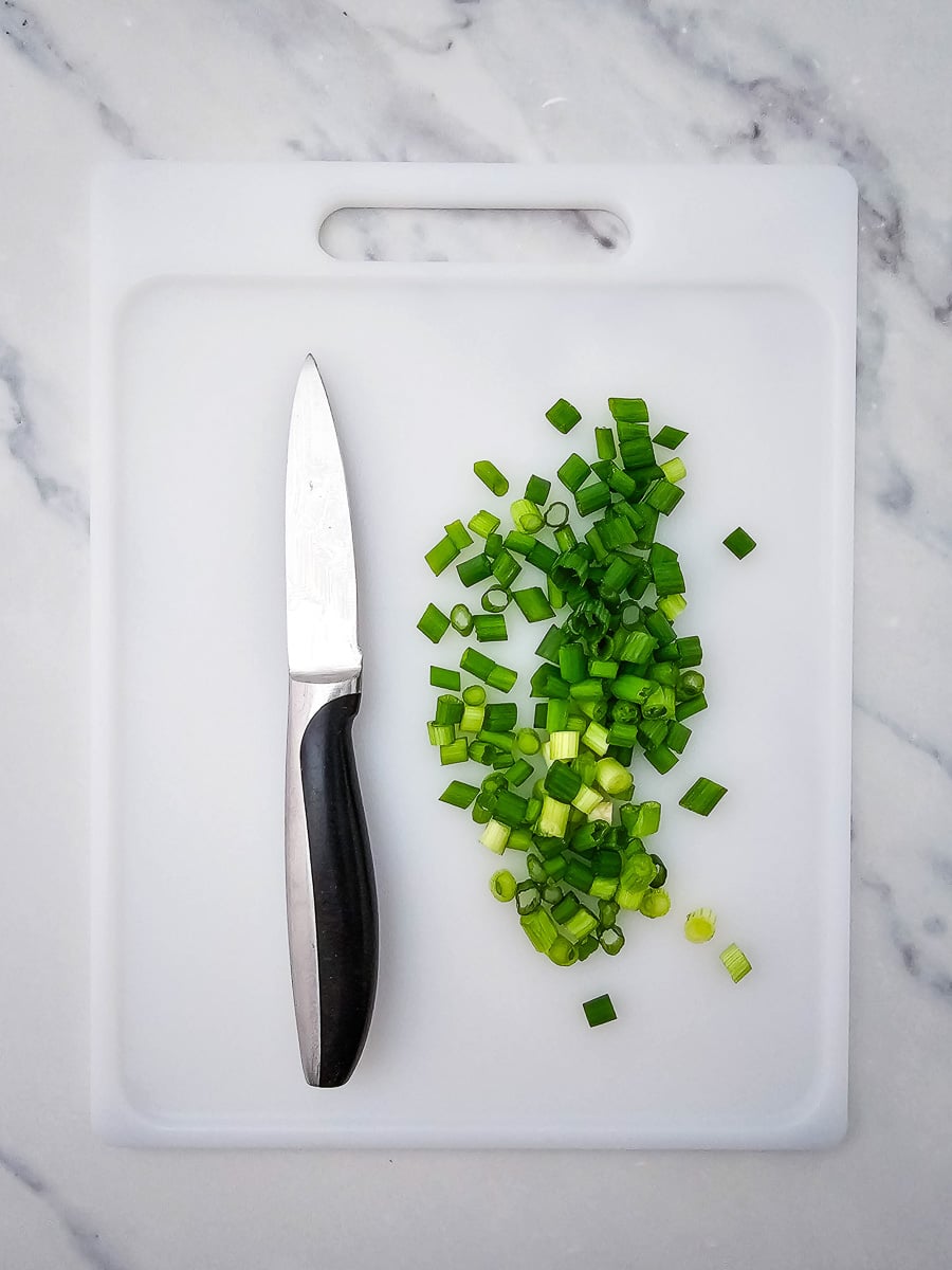 Green onion chopped on cutting board with knife on the side.