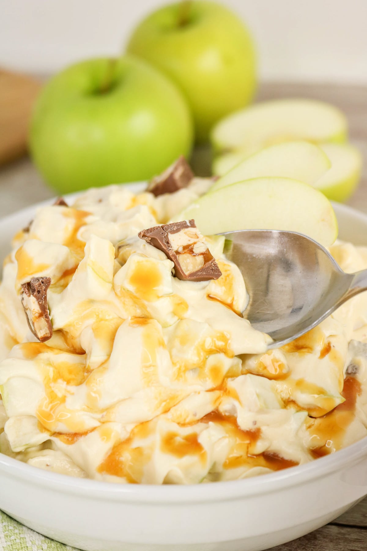 Spoonful of apple Snickers salad held over bowl of dessert salad.