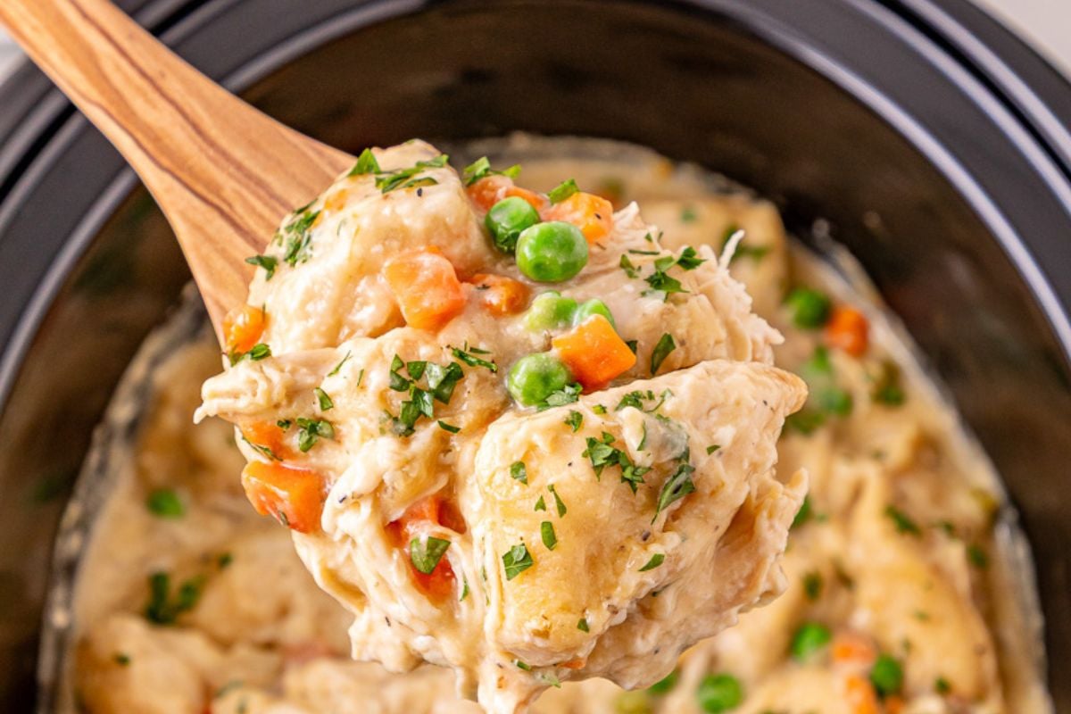 Crockpot chicken and dumplings scooped up on a spoon held over slow cooker.