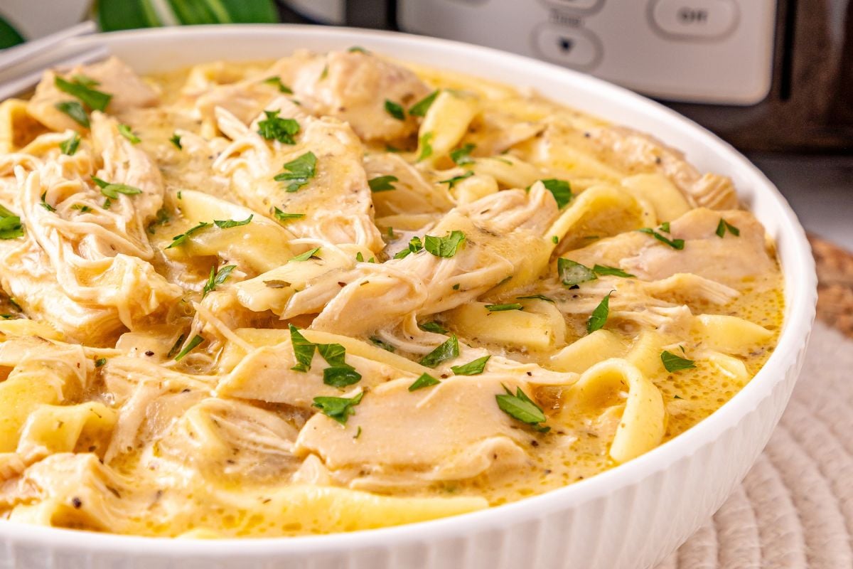 Crockpot chicken and noodles served in a white bowl.