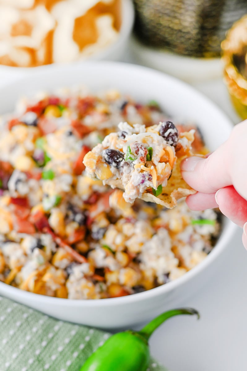 Loaded cowboy corn dip scooped up on a nacho chip and held over the bowl.