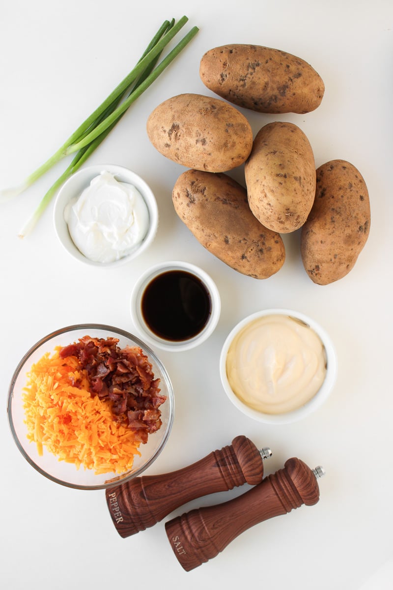 Ingredients for loaded baked potato salad laid out in small bowls on kitchen counter.