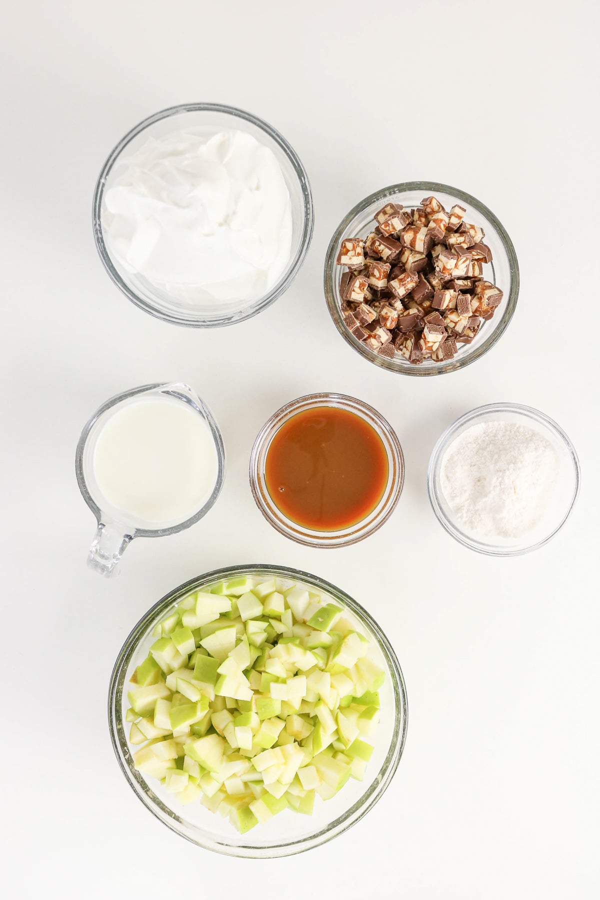 Ingredients for apple Snickers dip in small bowls on counter in preparation for the recipe.