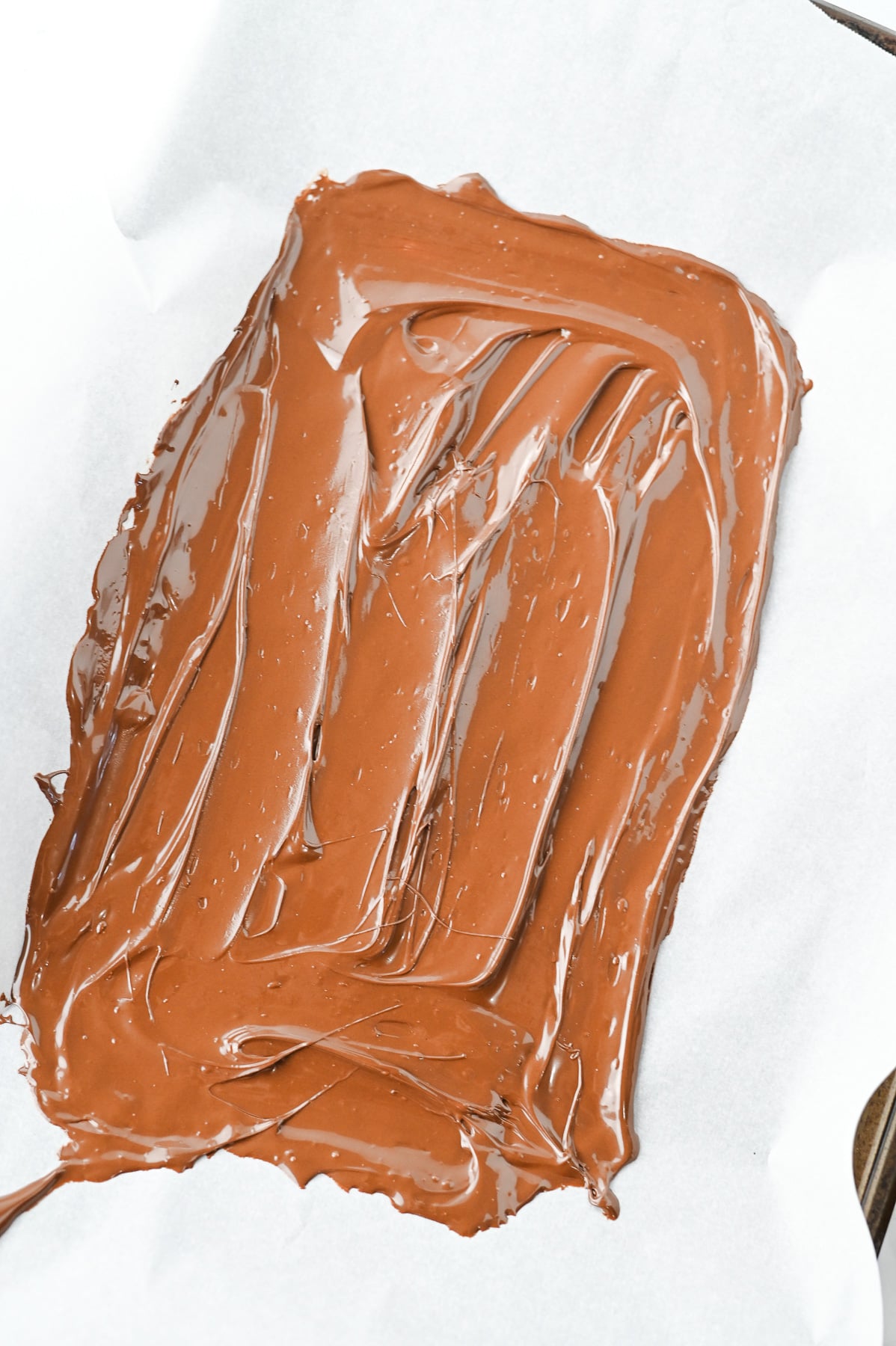 Melted chocolate spread out on parchement paper on baking sheet.