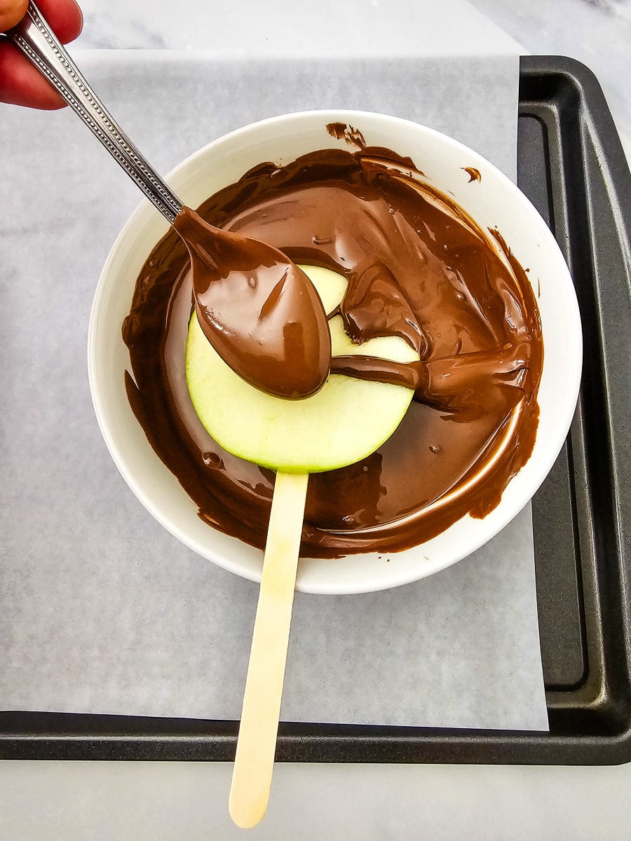 Apples on stick are dipped into melted chocolate.