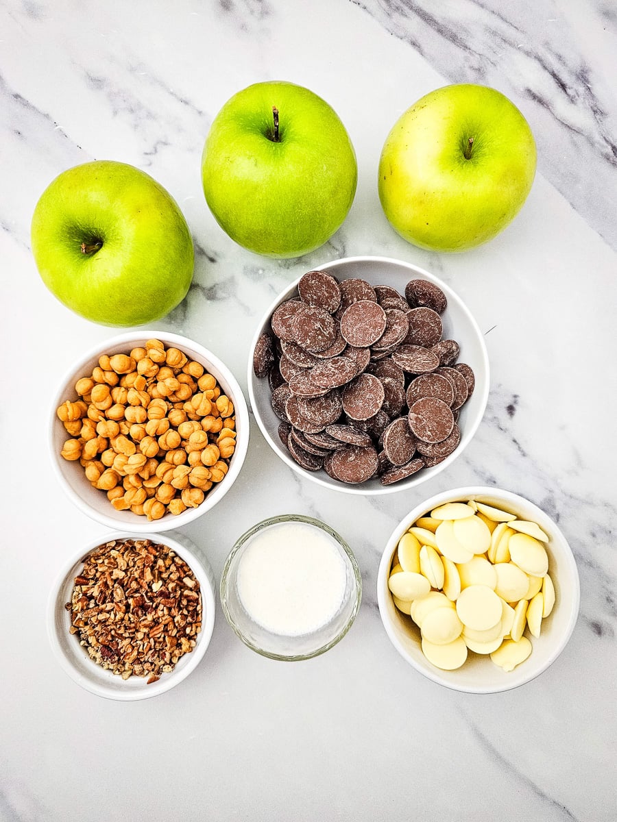 Ingredients for chocolate caramel apple slices laid out in small bowls on counter.