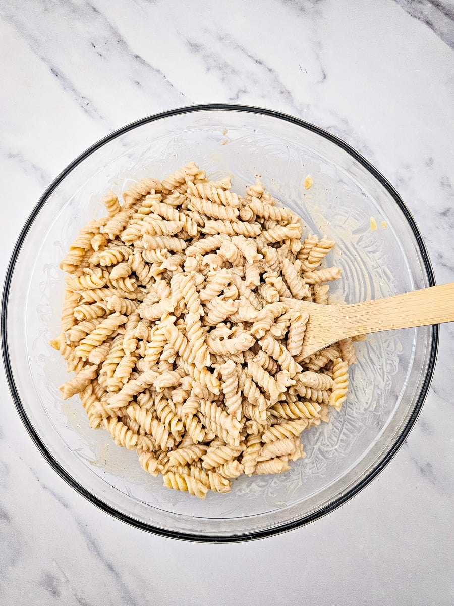 Cooled pasta is tossed with dressing in large mixing bowl.