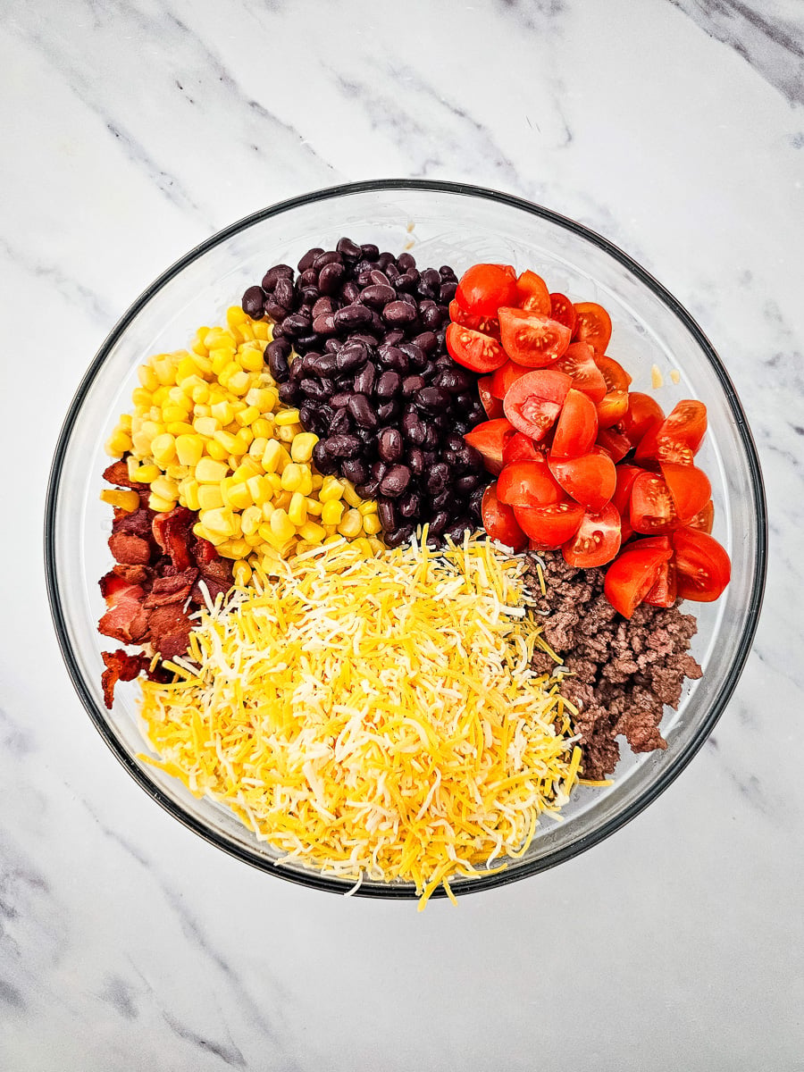Cooked ground beef, bacon, black beans, corn, tomatoes, shredded cheese, and green onions added to mixing bowl.