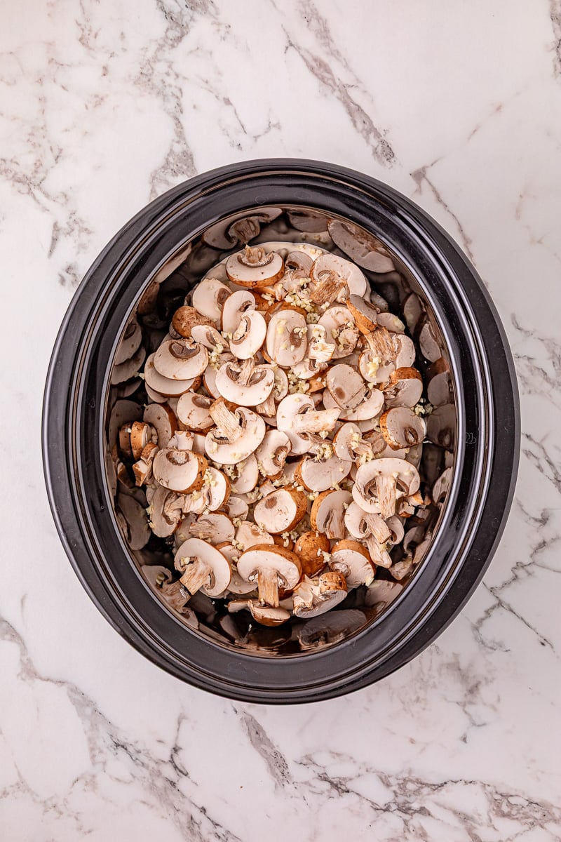 Fresh sliced mushrooms are spread on top of chicken and mushroom sauce mixture in slow cooker.