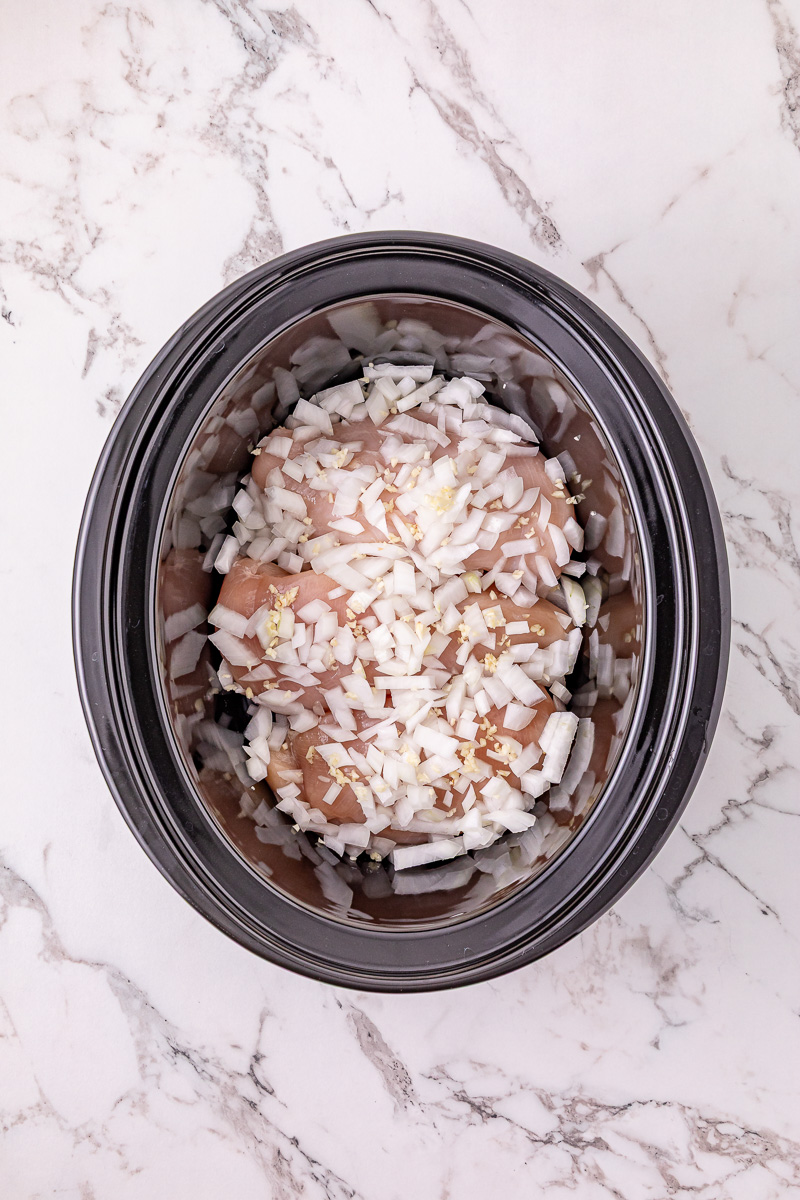 Garlic and onions are added to the top of the crockpot.