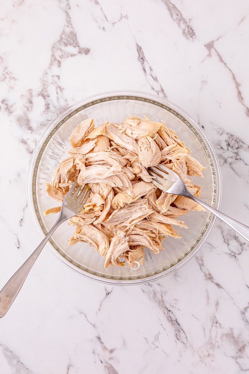 Chicken is shredded with two forks in small mixing bowl.