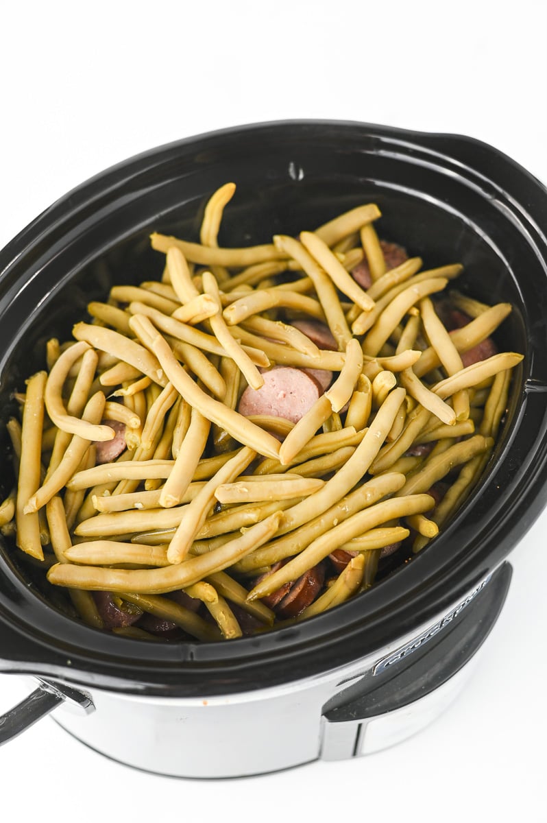 Green beans are added to the top of the potato sausage mixture for the final phase of cooking.