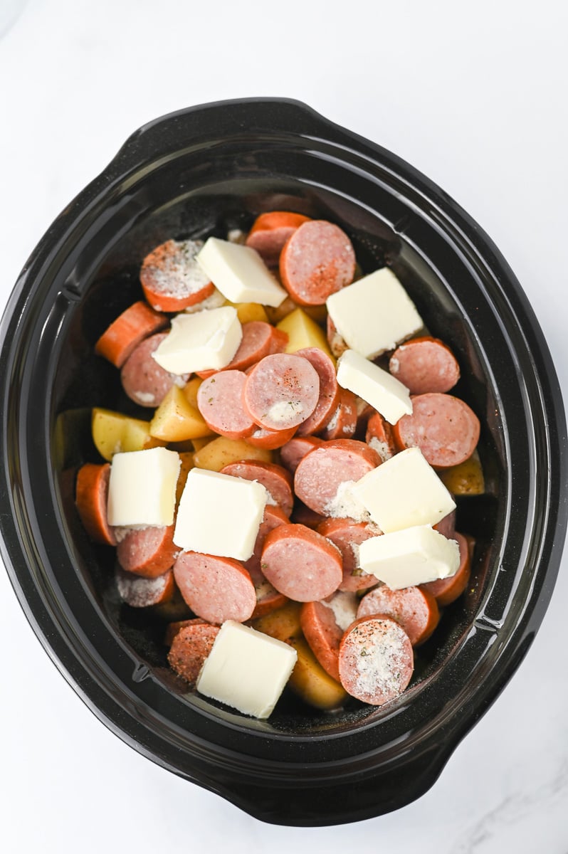 Sliced stick of butter is added to the top of the mixture in crockpot.
