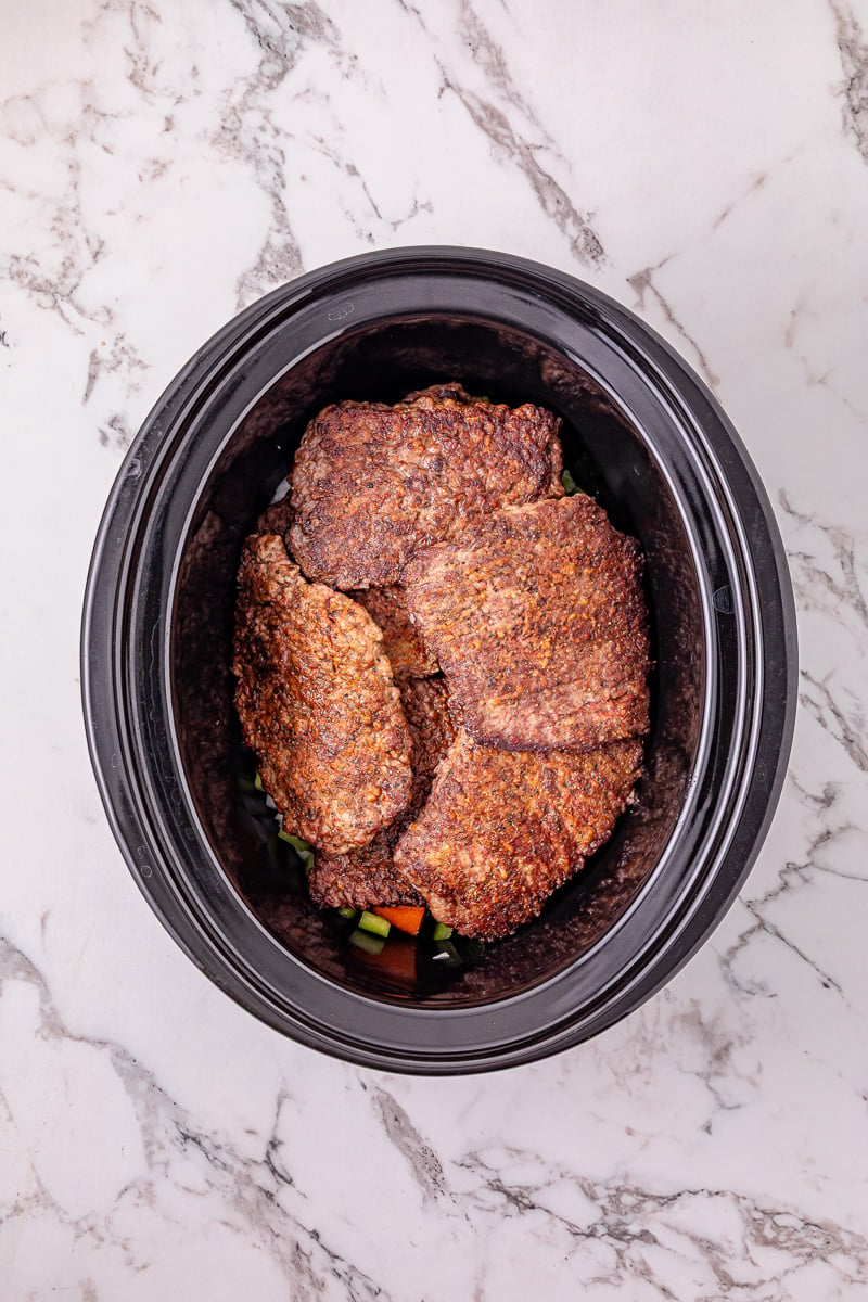 Seared steaks are placed on top of the veggie mixture.