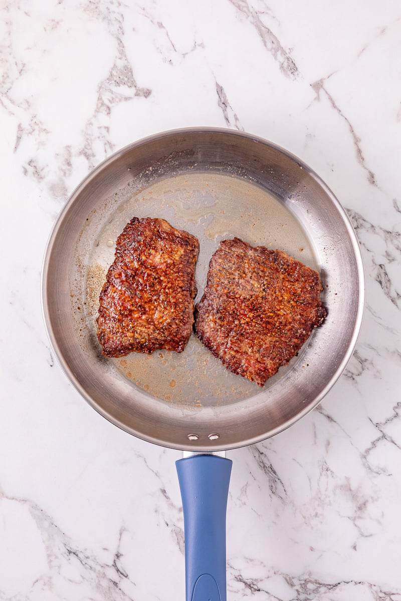 Steaks in pan searing for the recipe.