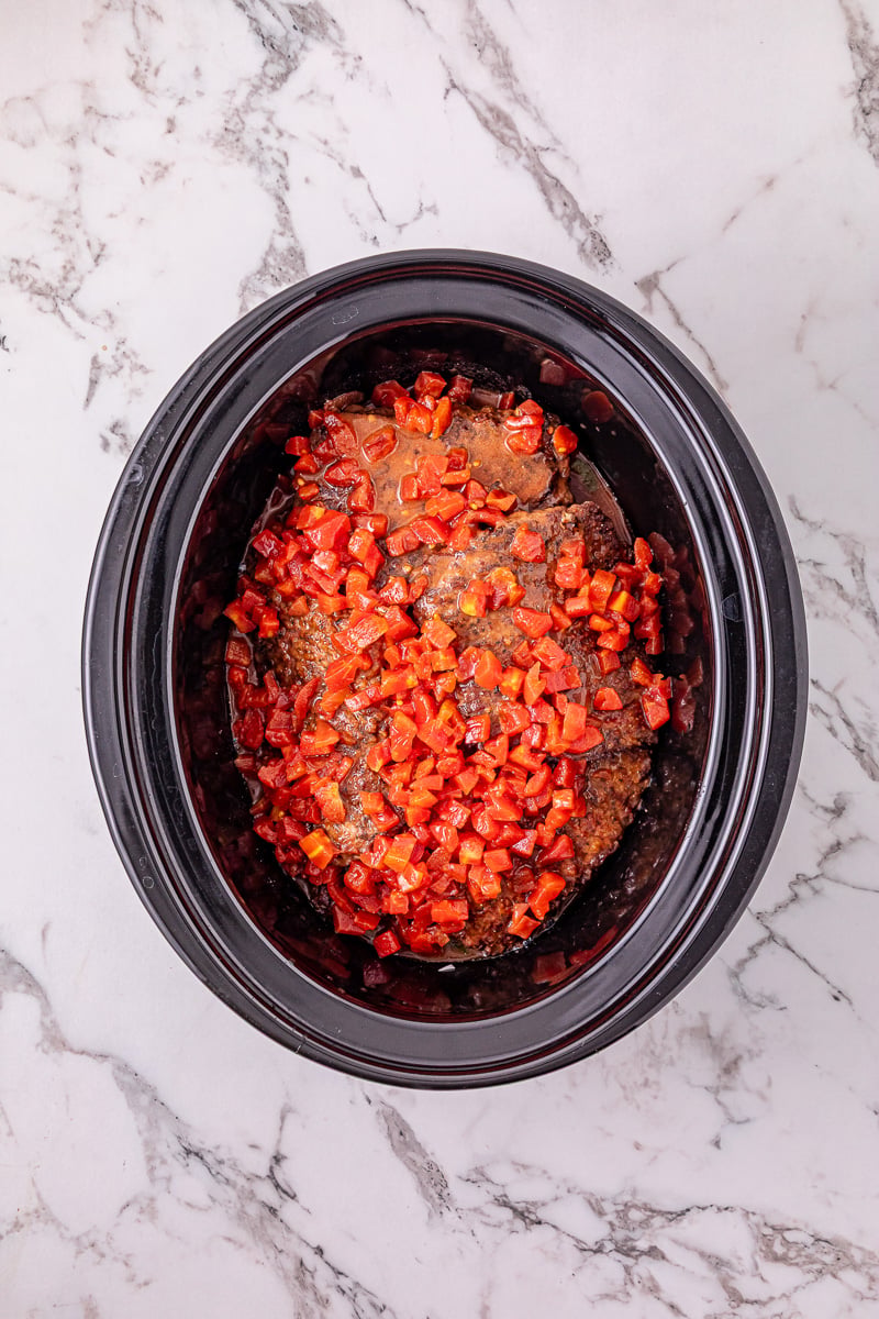 Tomato mixture is sprinkled on top of the steak in crockpot.
