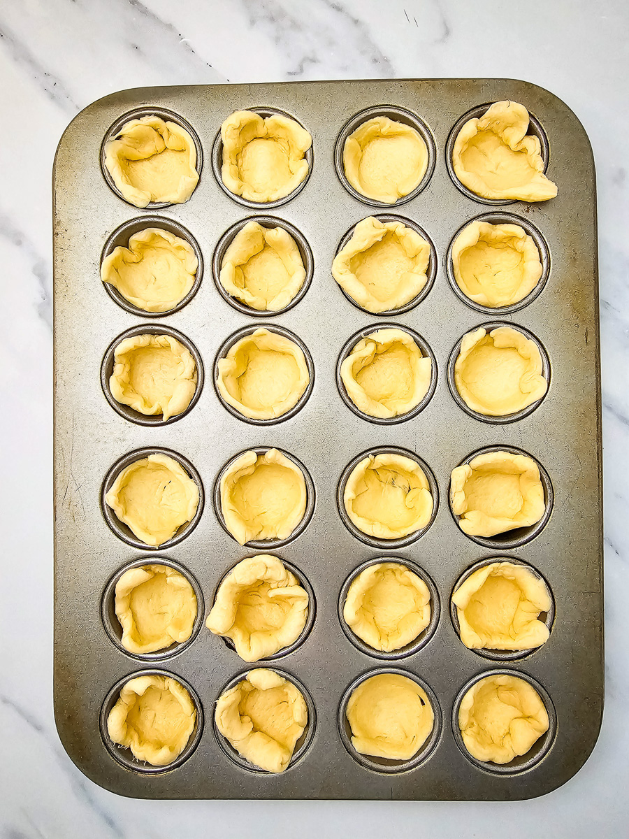 Crescent roll dough is pressed into the bottom of mini muffin tin.