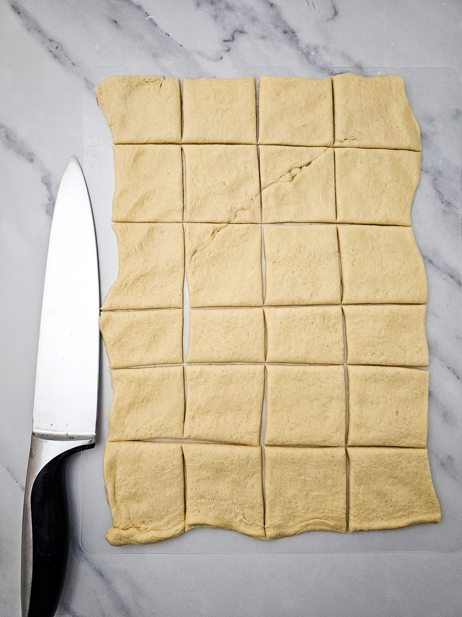 Crescent roll dough is cut into squares on counter.