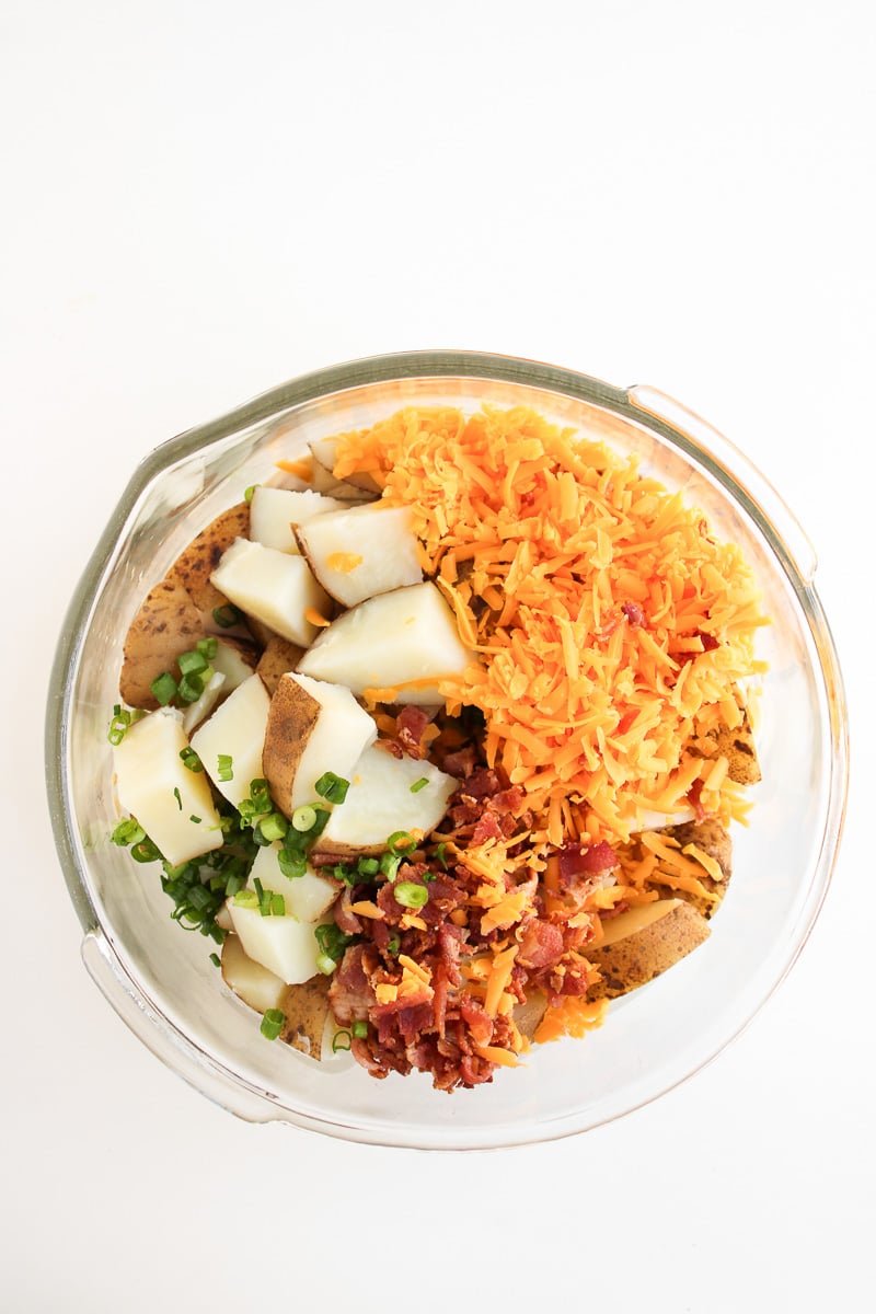 Cooled potatoes, shredded cheese, crumbled bacon, and green onion are added to the bowl with potatoes.